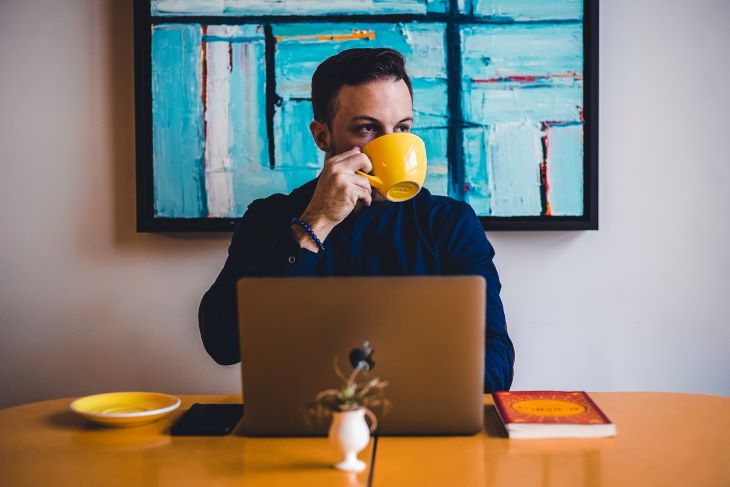 A man on his laptop drinking coffee at drug and alcohol rehab in Bedfordshire