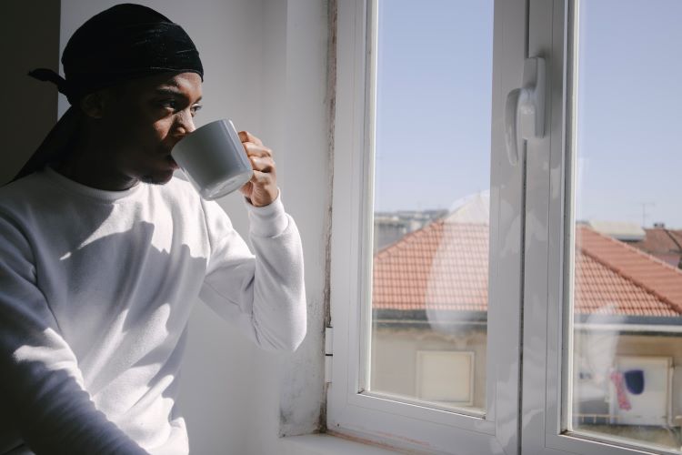 A man looking out of a window drinking tea