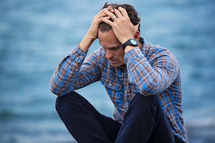 Man holding his head and sat next to a lake at a drug and alcohol rehab centre in Edinburgh