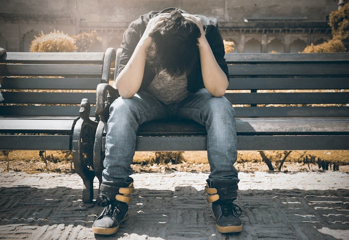 Man sitting on bench holding his head in his hands