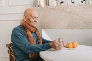 Old man sitting at a table holding a drink at rehab