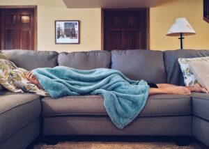 Person lying on a sofa underneath a blanket in Milton Keynes