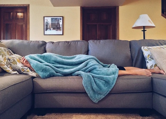 Person lying on a sofa underneath a blanket