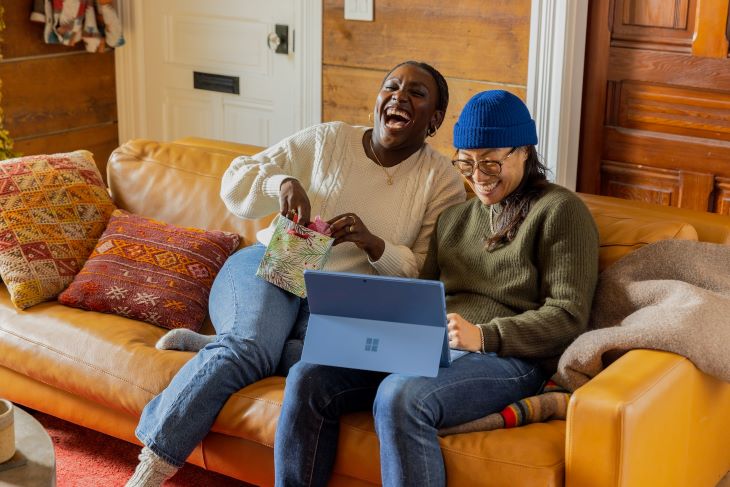 two people sat on sofa with open laptop, laughing