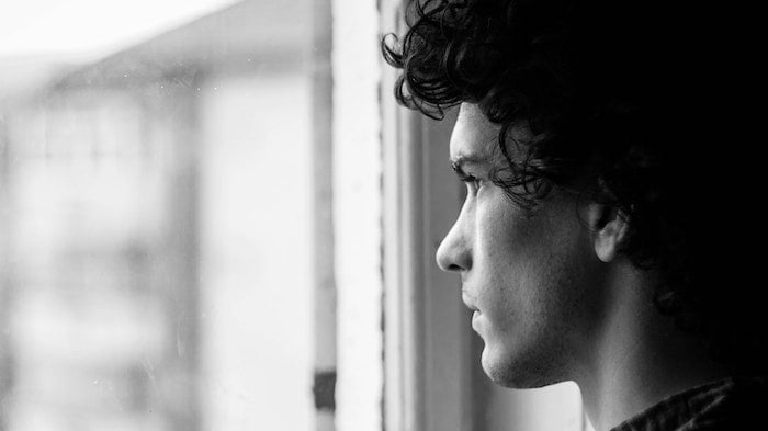 Black and white photo of a young man looking out of a window at a drug and alcohol rehab clinic in Durham