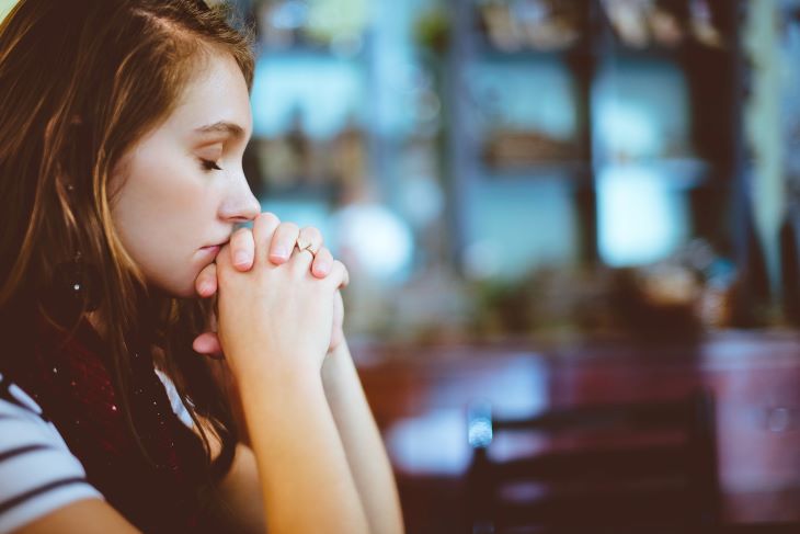 A woman with her hands clasped, eyes shut