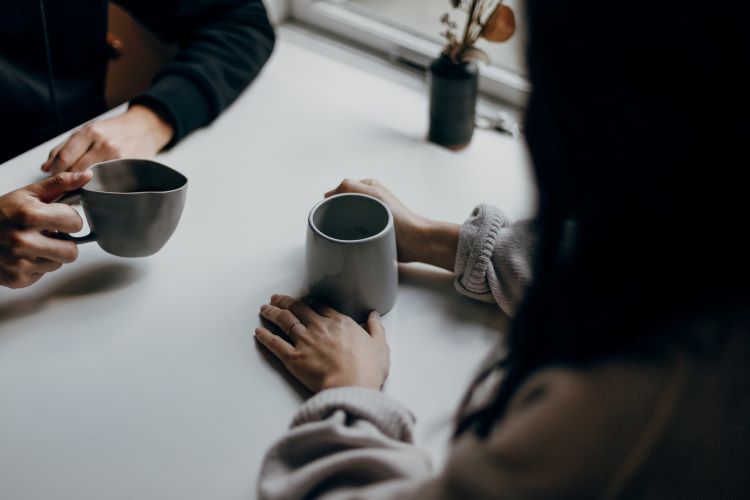 Two people talking at a table with mugs