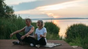 Two people sitting on the floor meditating by a lake