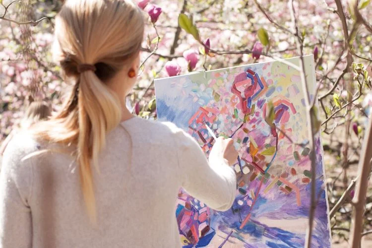 A woman painting at art therapy, with pink flowers behind her