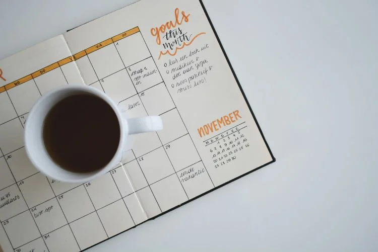 A paper calendar with added goals. A black coffee on top