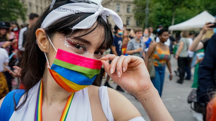 A woman at a pride parade wearing a rainbow mask and glitter makeup