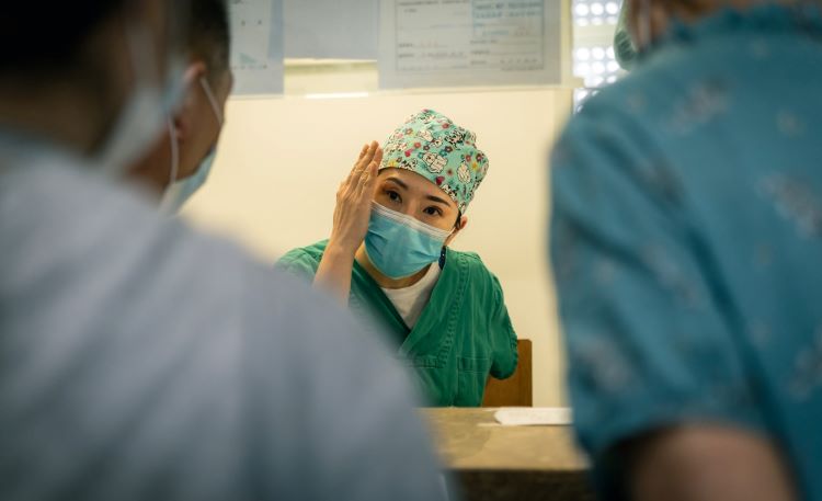 Nurse in deep thought wearing a mask and scrubs and talking to others