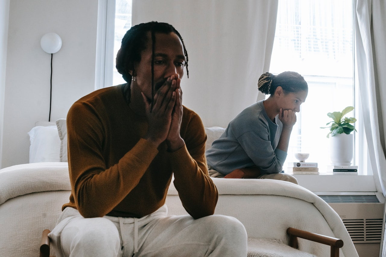 A couple sitting in a bedroom looking fraught