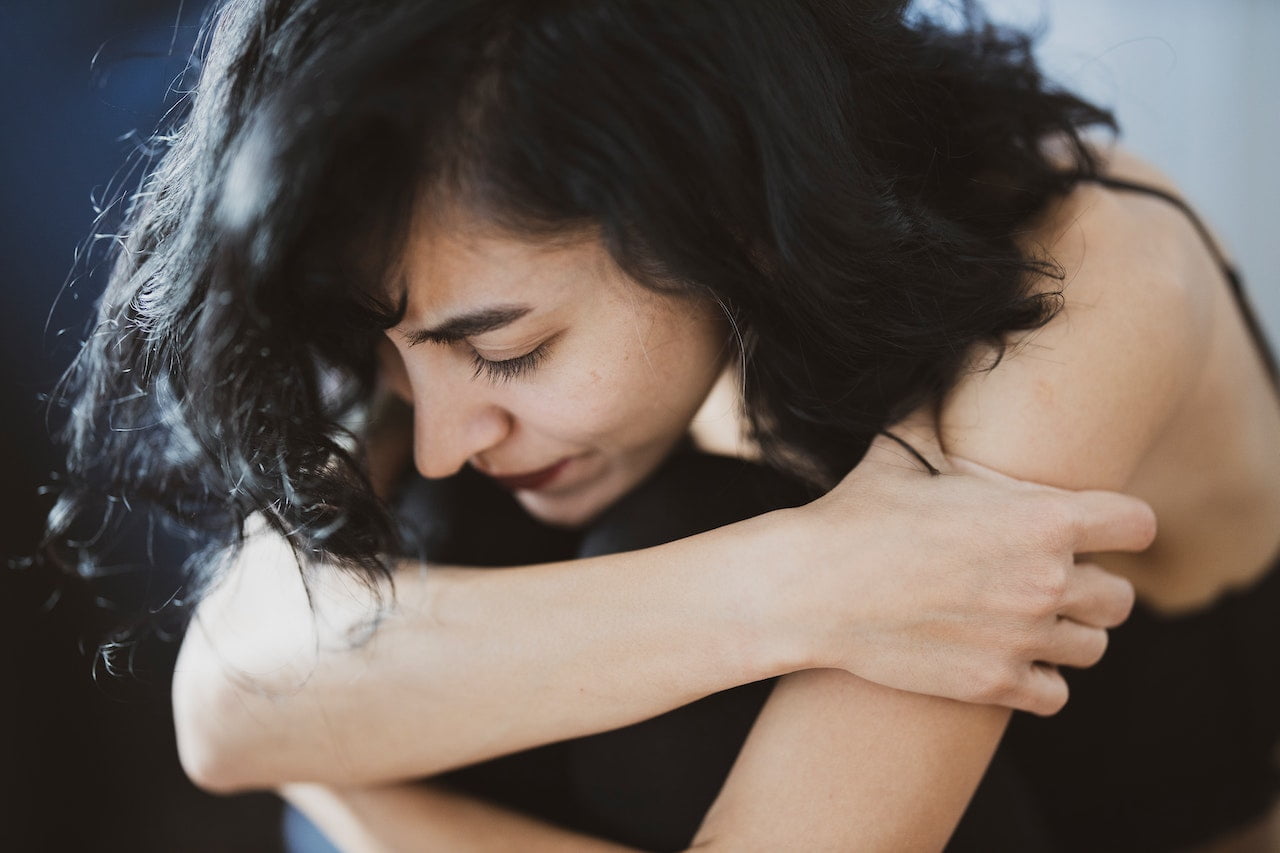 A woman in a crouched, defensive pose with her arms around herself, considering inpatient or outpatient rehab