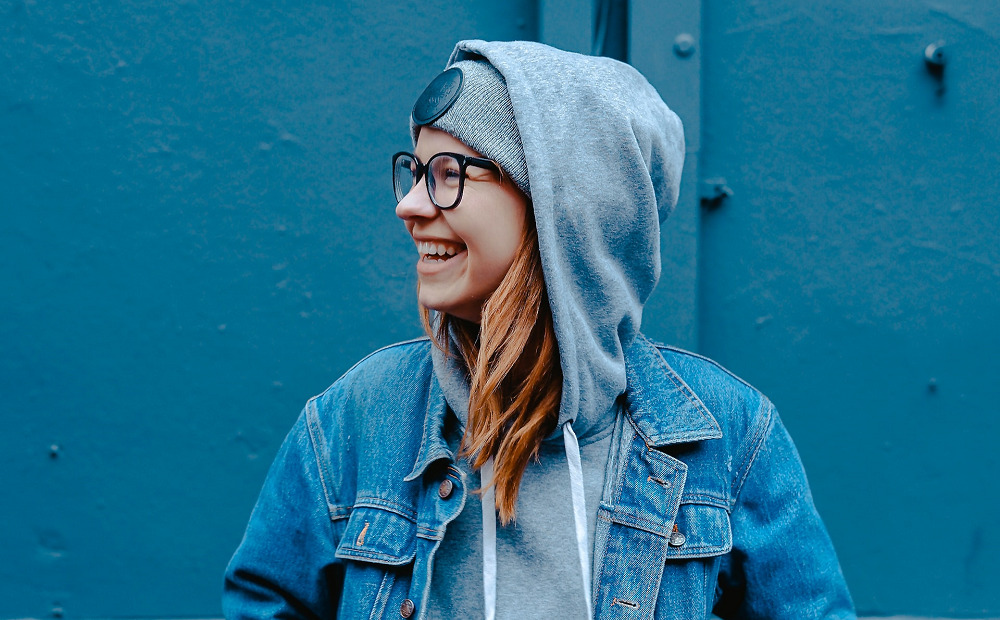 A young woman in recovery smiling in a hoodie and glasses