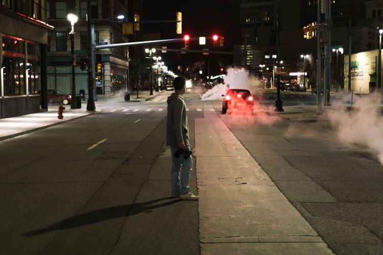 A man standing on a traffic light-lit street at night