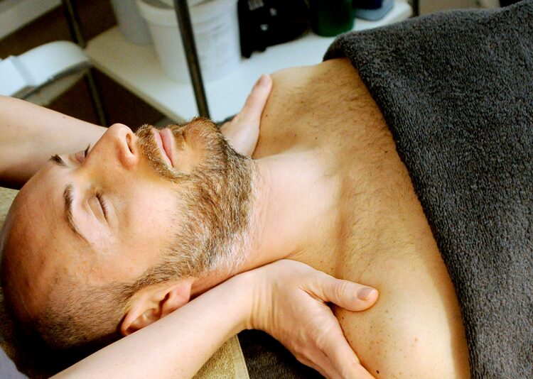 A man at a spa wearing a towel with a therapist's hands on his shoulders
