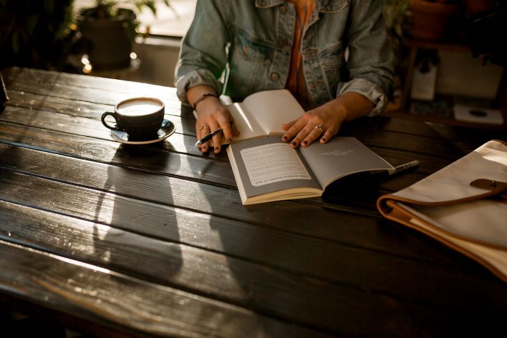 Person reading and taking notes and drinking a coffee