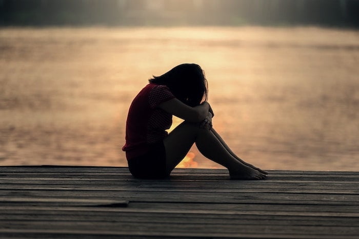 Woman sat next to a lake holding her legs and thinking about postpartum depression